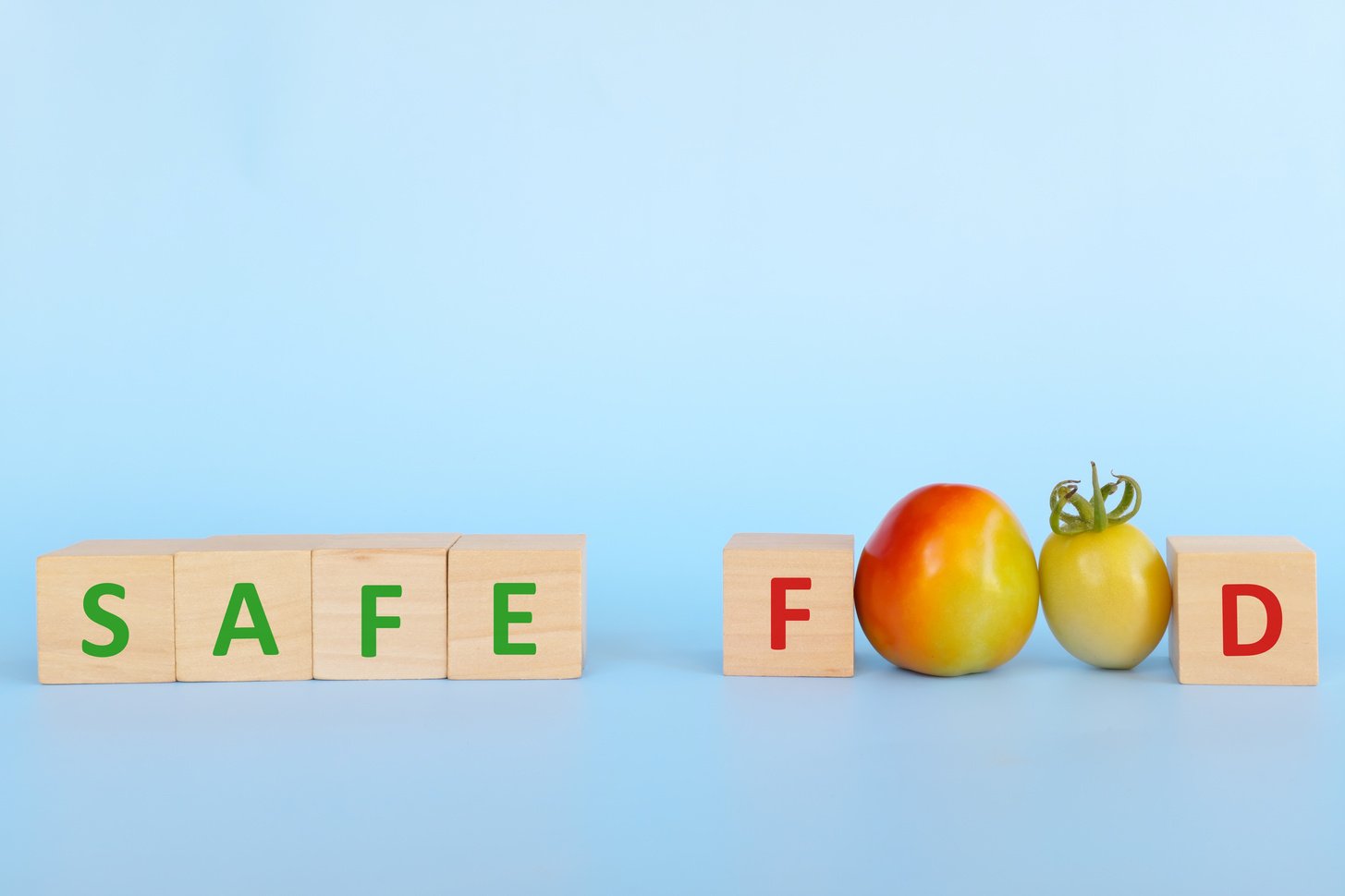 Safe food concept. Tomato and wooden blocks with word safe food on blue background with copy space.